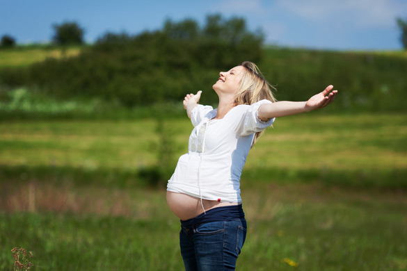 Happy-pregnant-woman-with-arms-outstretched-enjoying-sunlight-at-field